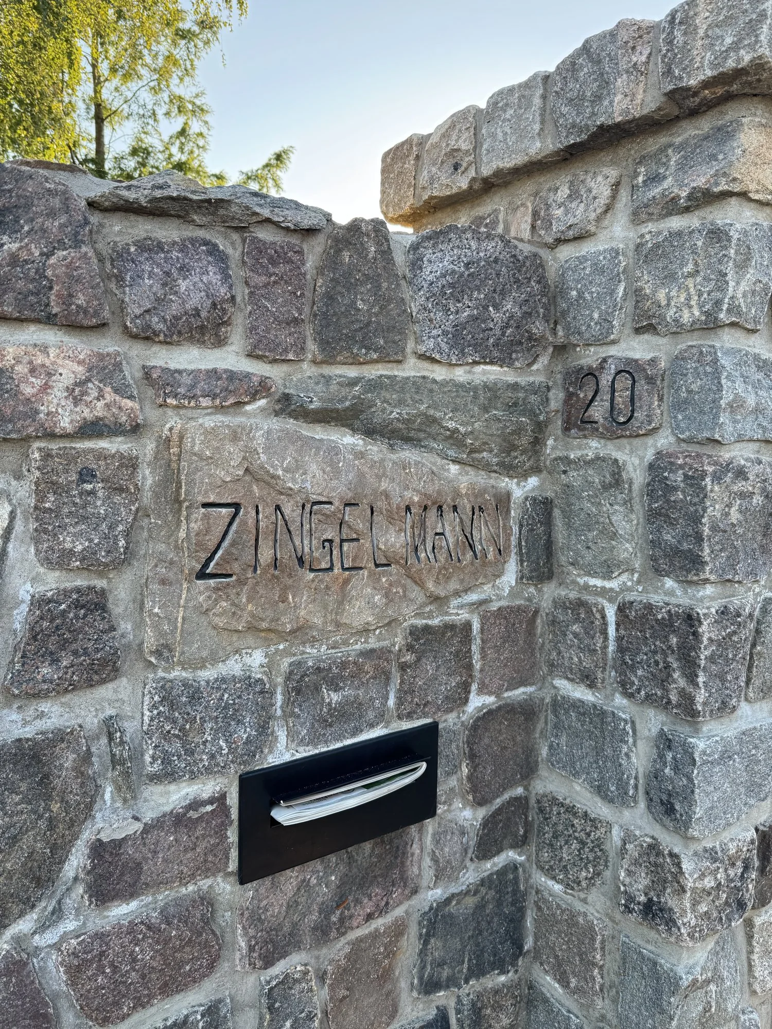 Gravierter Familienname Zingelmann und Hausnummer 20 in einer Natursteinmauer