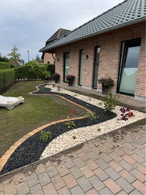 Geschwungenes Gartenbeet mit hellem Zierkies und dunklem Lavastein