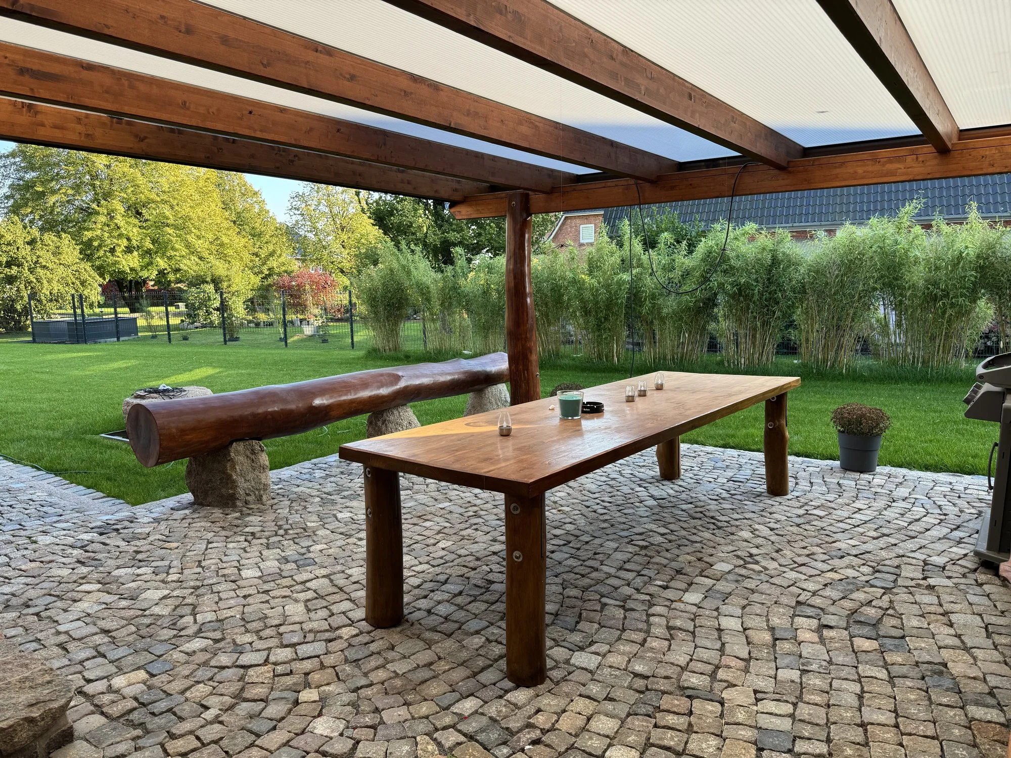Holztisch und Bank auf der überdachten Terrasse mit Natursteinpflaster