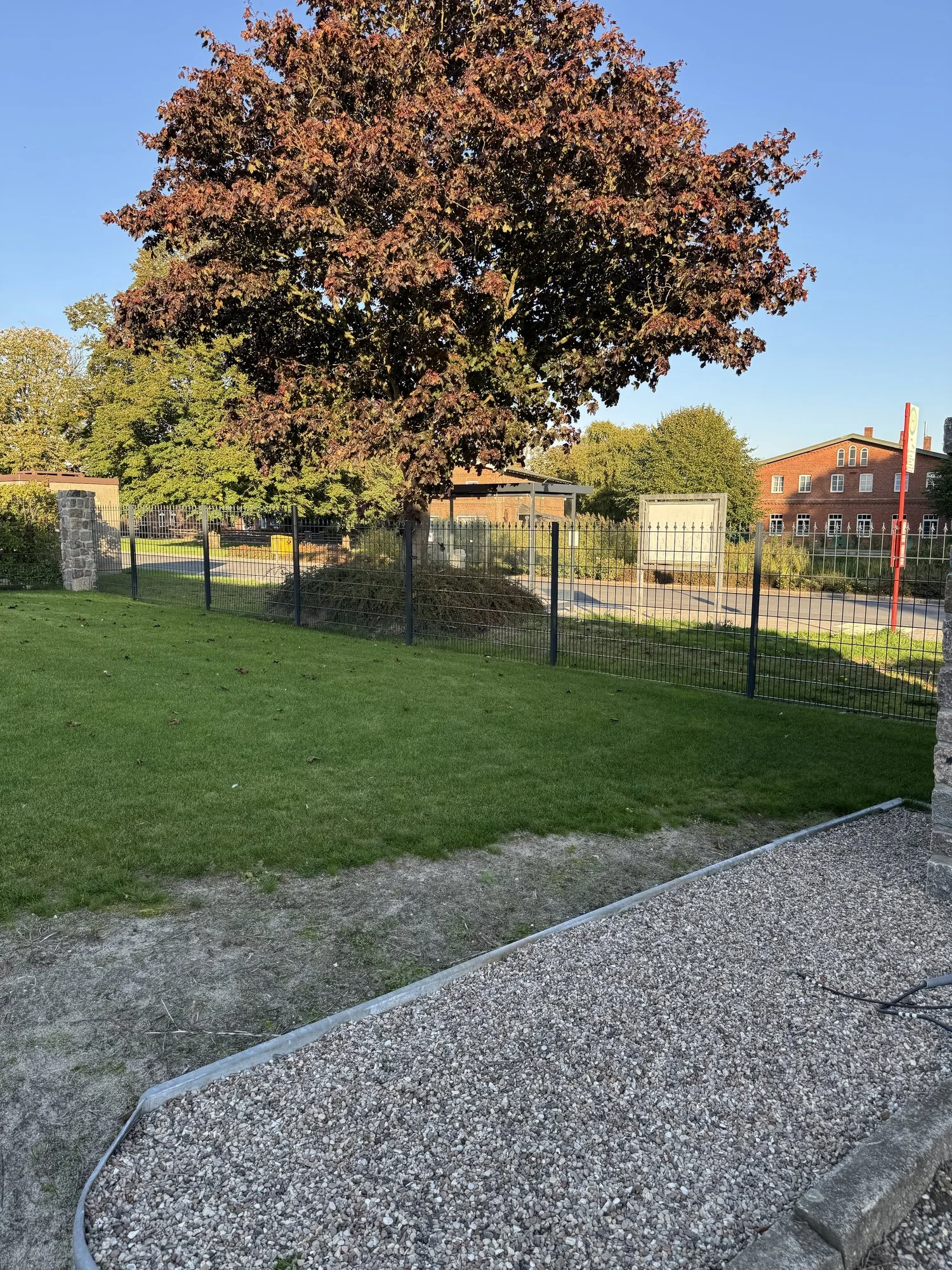 Dunkler Metallzaun entlang der Grundstücksgrenze mit Baum und Kiesbeet