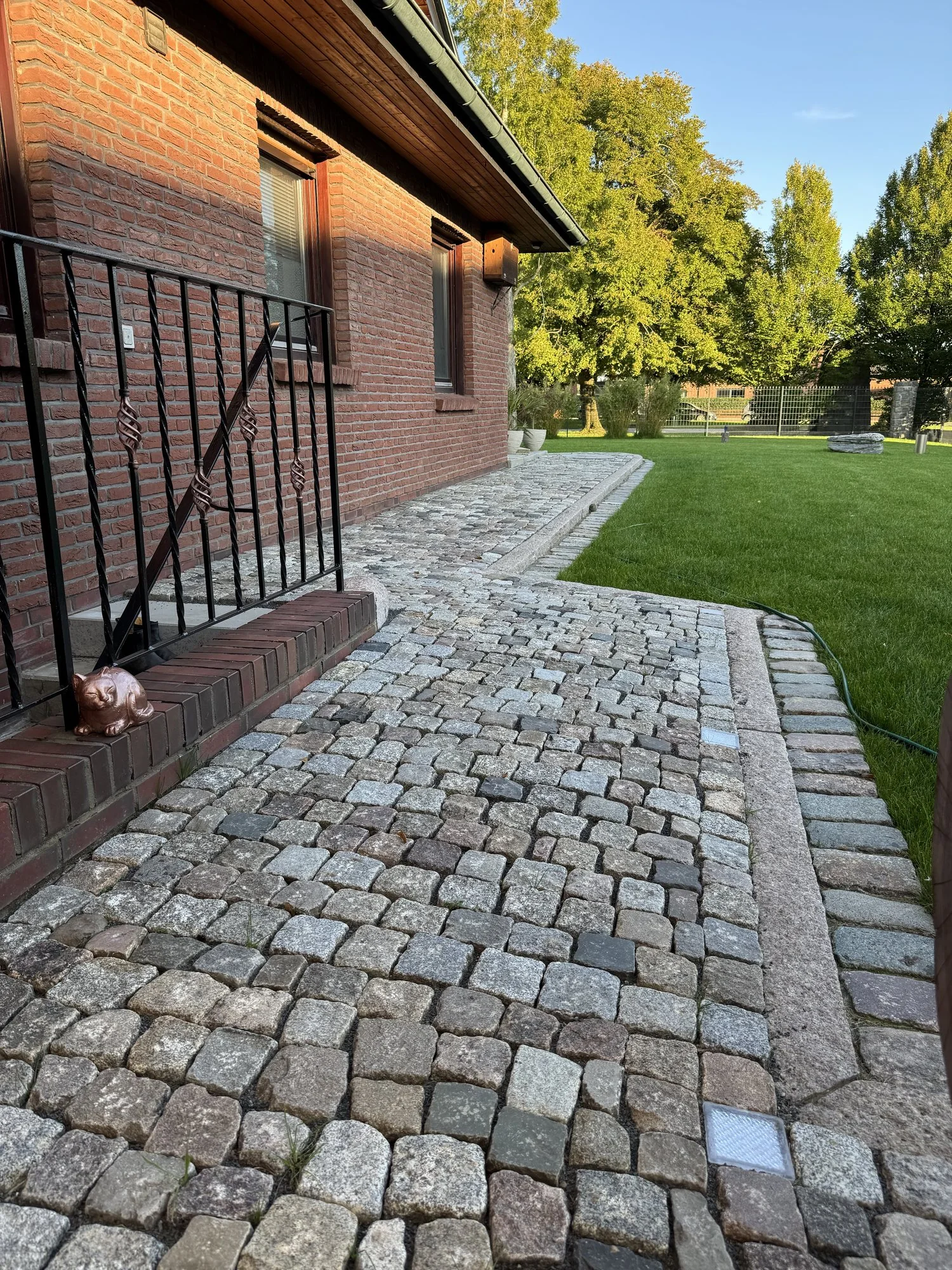 Natursteinpflaster entlang eines Hauses mit Beeteinfassung und Rasen
