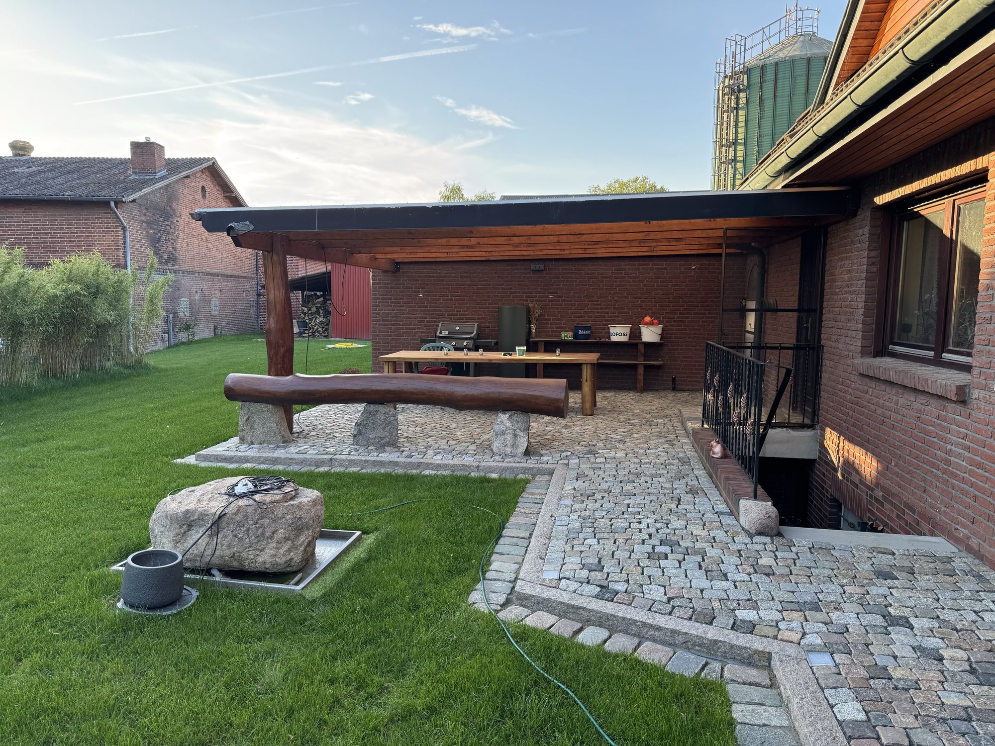 Garten mit überdachter Terrasse, Rasenfläche und Natursteinpflaster